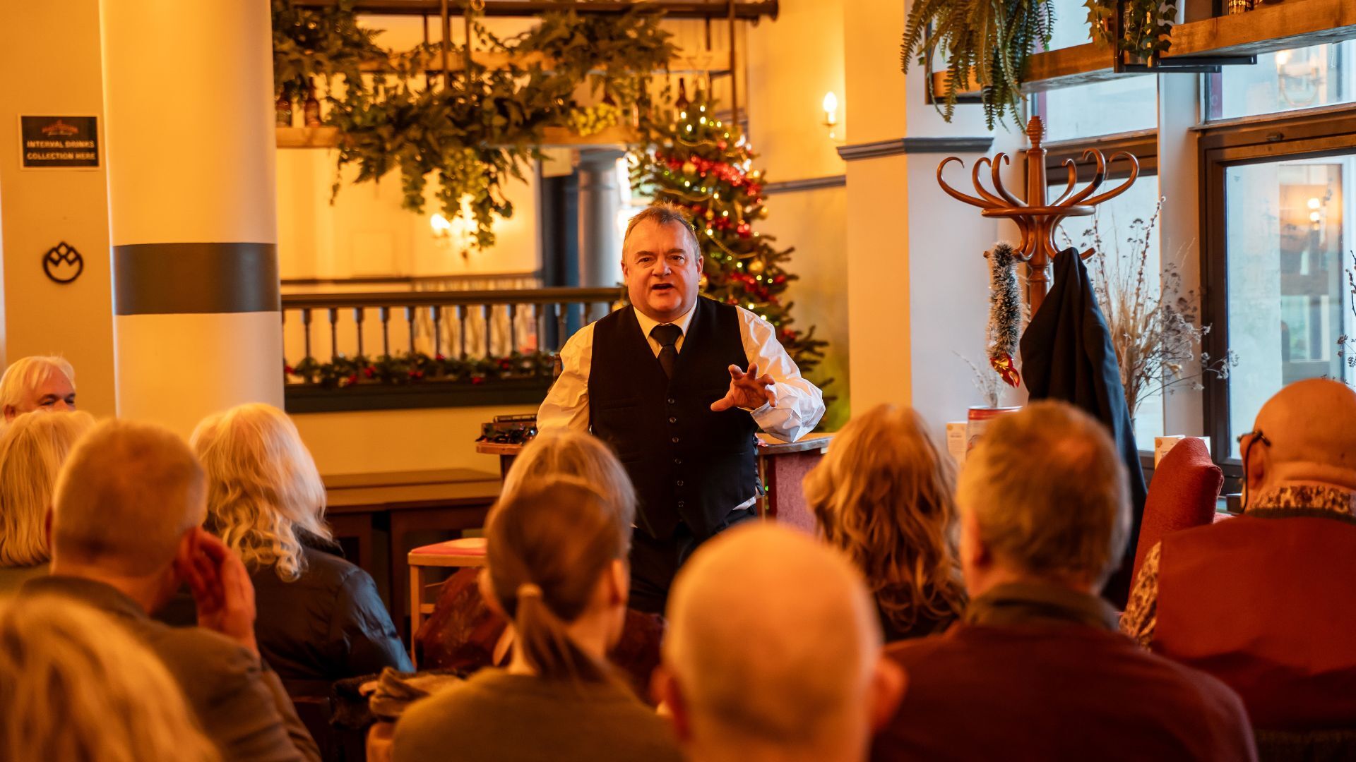 Man performing in front of a live audience with a Christmas tree and Christmas decoration in the background