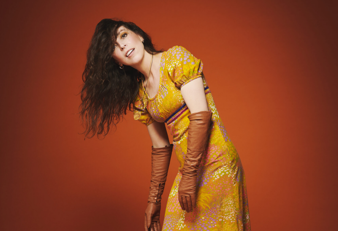 Bridget Christie in a yellow dress leaning to her side
