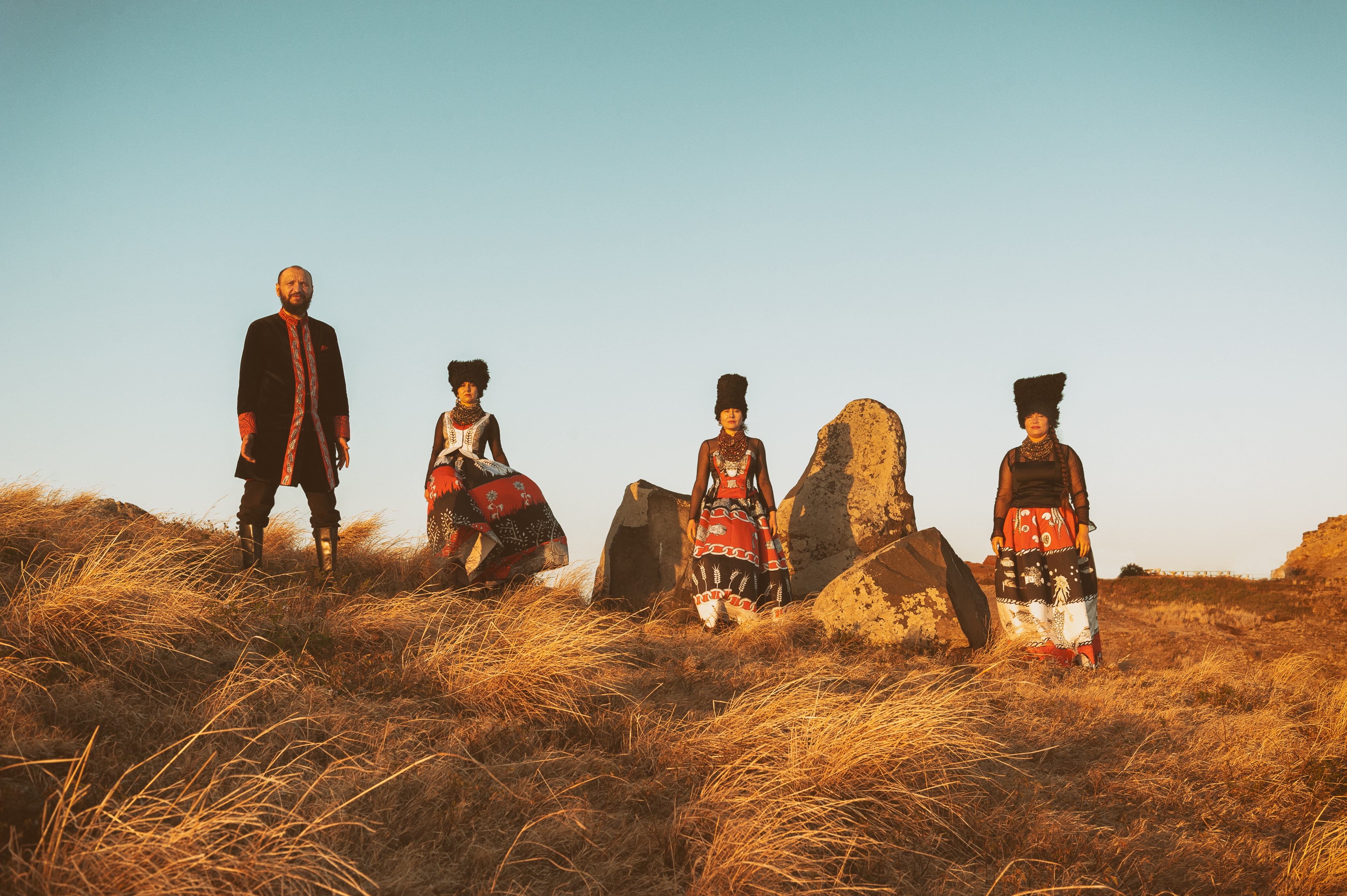 Photo of the band DakhaBrakha standing on grass with a blue sky behind them