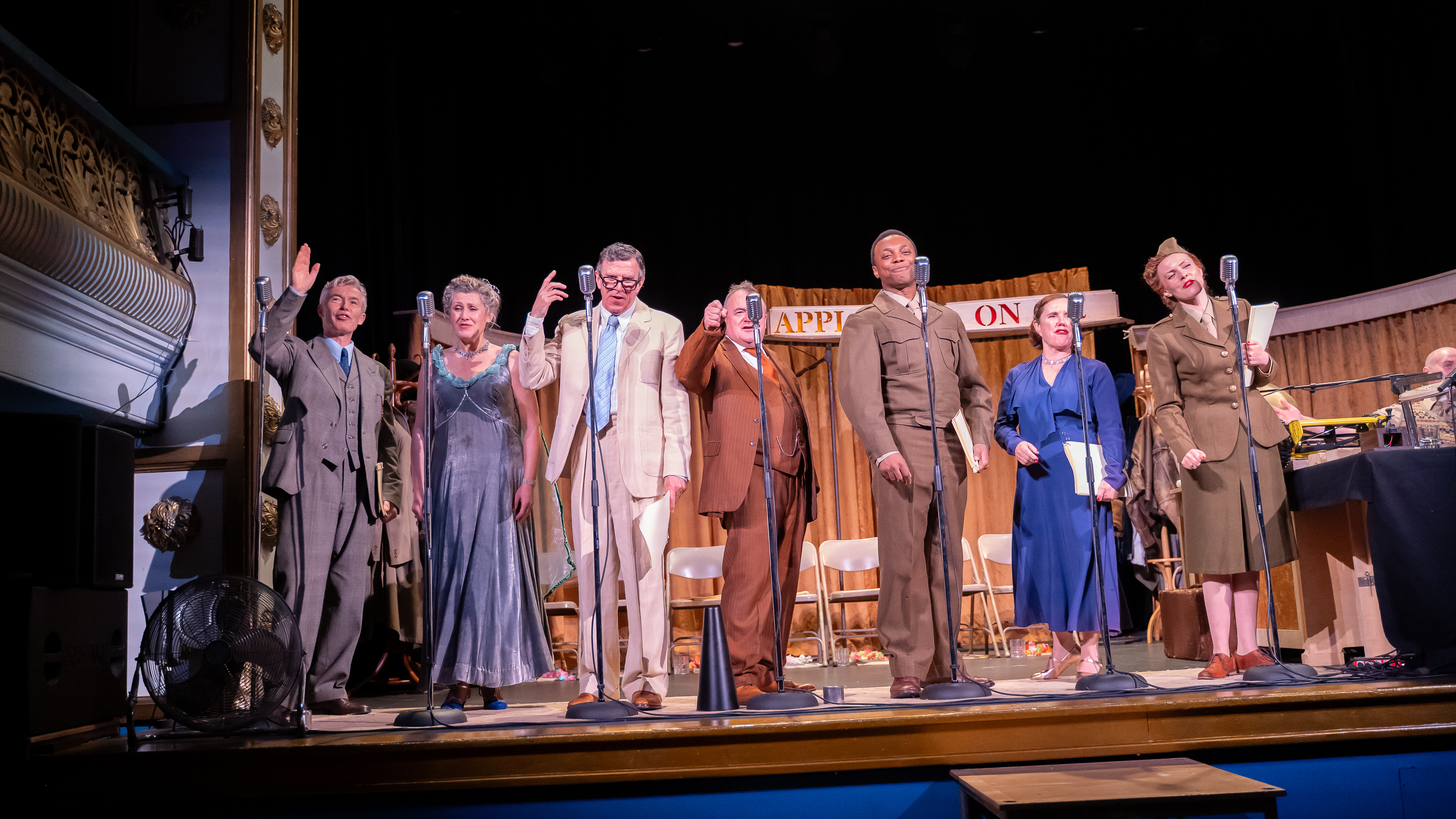 Cast of the show dressed up standing in a line in front of mics