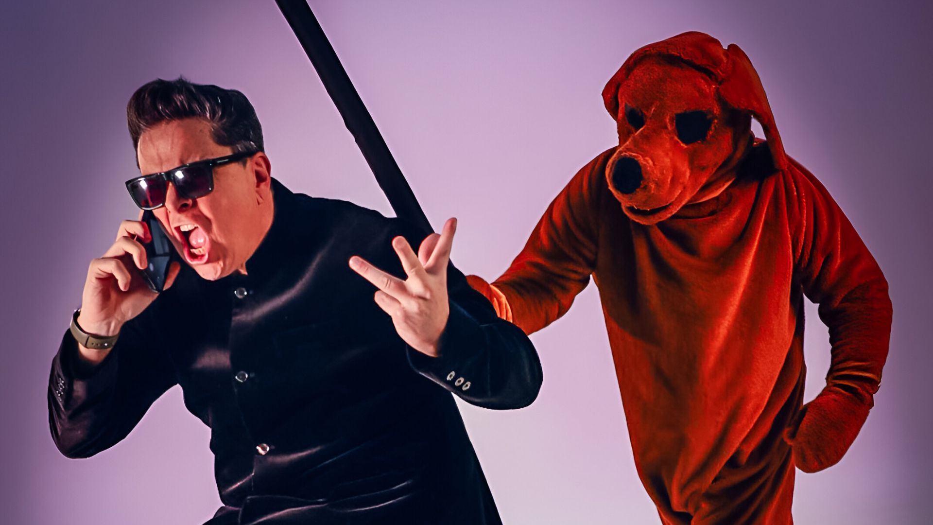 Man dressed in black on the phone with someone dressed up as a dog coming after him