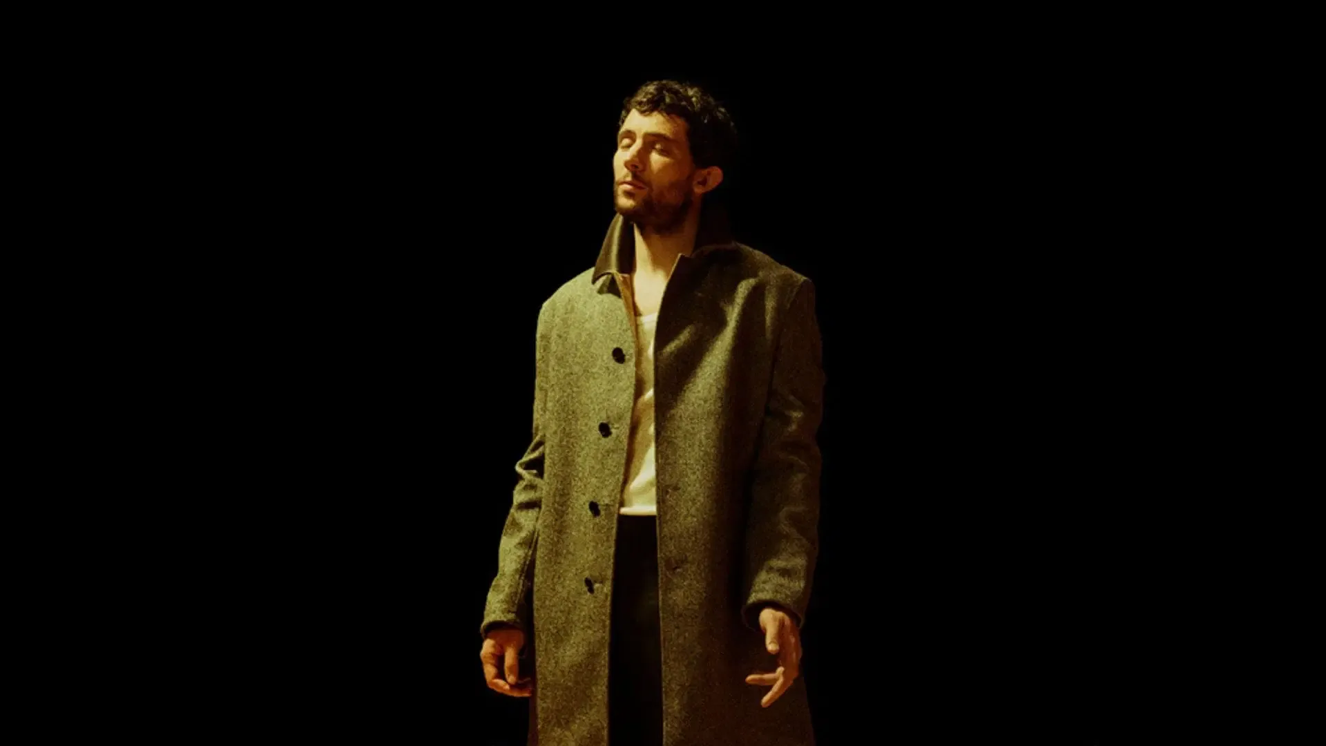 Man wearing a long coat standing with his eyes closed