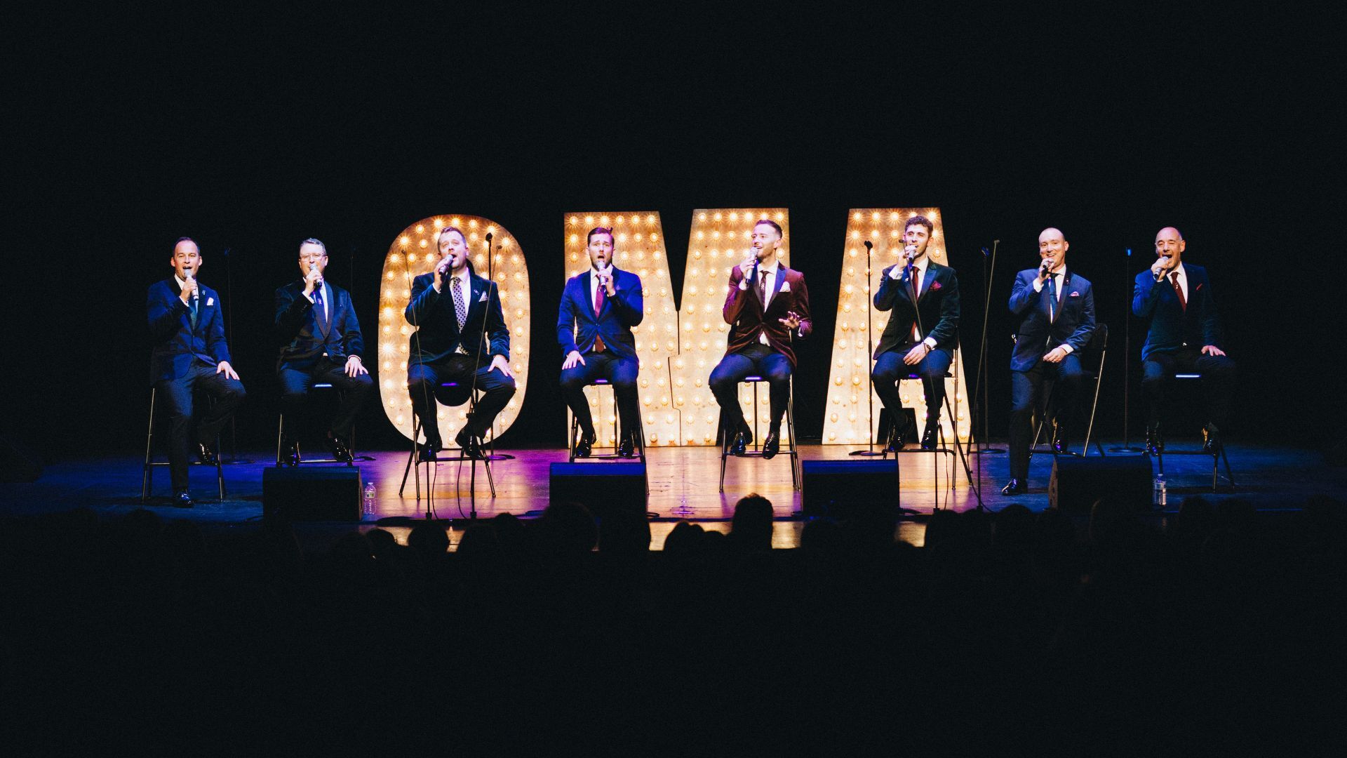 Only Men Aloud on stage singing with OMA letter behind them