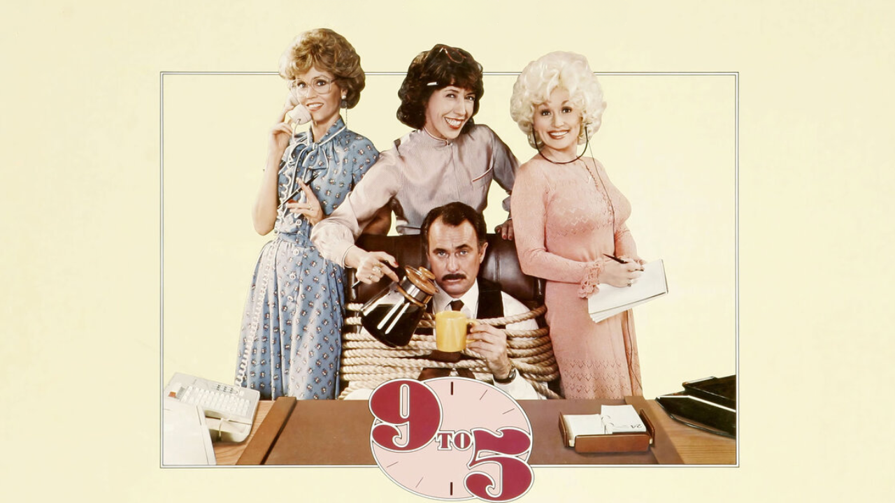 three women working, answering the phone, taking notes and pouring coffee and a man with a rope around him stuck in an office chair