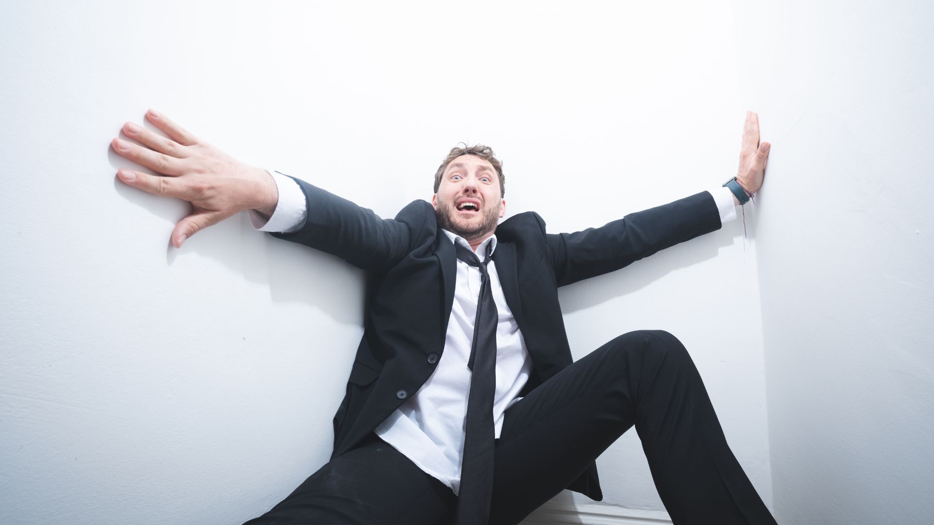 Seann Walsh wearing a suit an tie leaning back against a white wall as if he's in shock