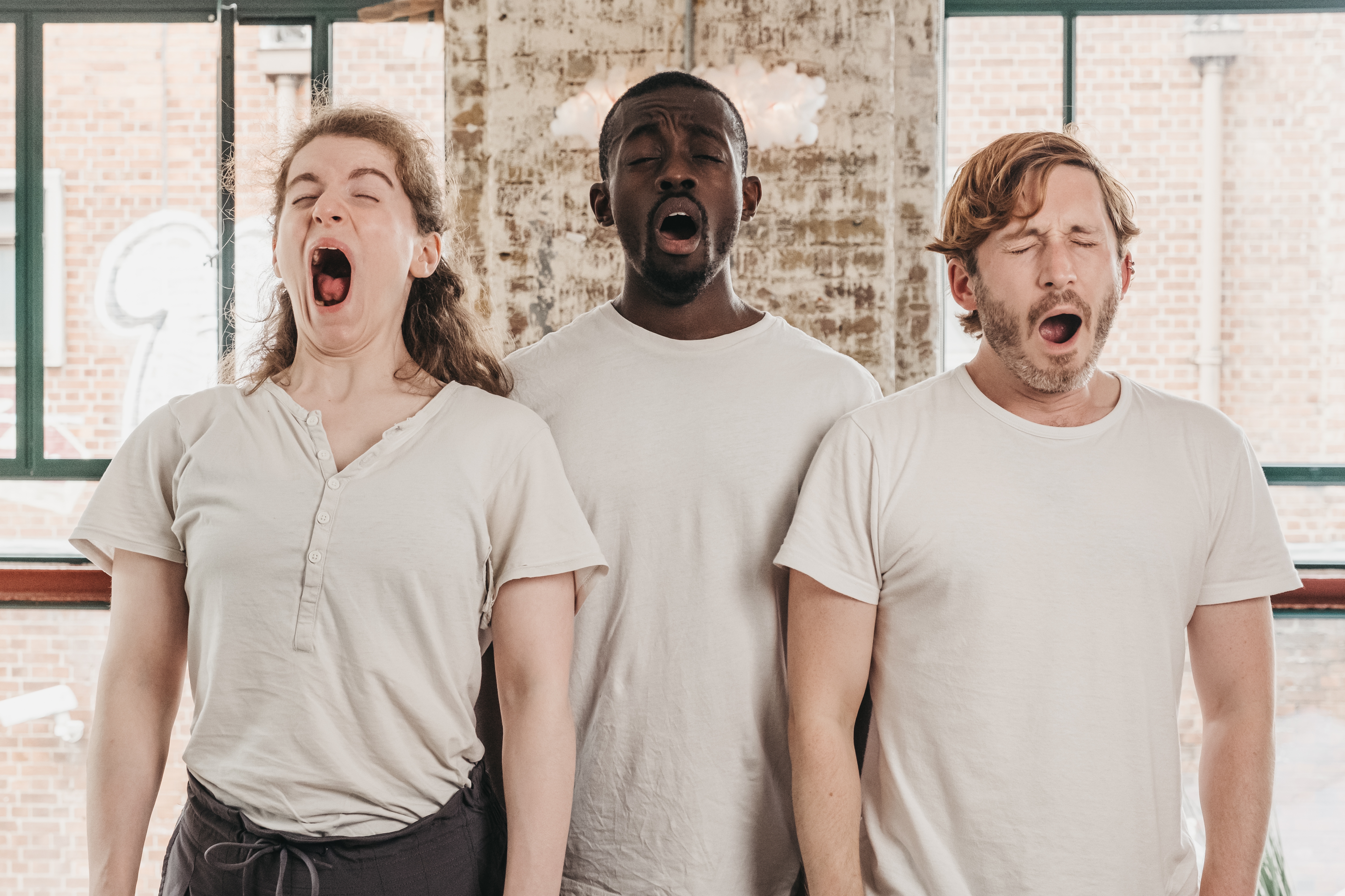 One woman and two males in cream coloured t-shirt yawning
