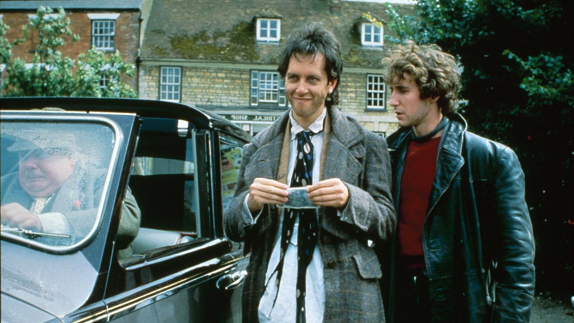 Withnail and Marwood standing near Monty's car in a village