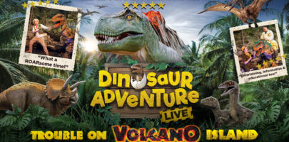 A vibrant dinosaur adventure poster set in a lush tropical jungle, featuring a roaring T. rex, Triceratops, flying pterosaurs, and live dinosaur performers. Bold yellow lettering promotes “Dinosaur Adventure Live!” and “Trouble on Volcano Island,” with fun testimonial photos and a dramatic family-friendly theme.