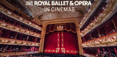 An image of a large and grand theatre with the red curtains drawn and a full audience