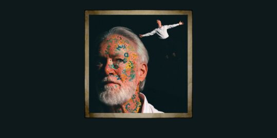 Close of a man with white hair and a beard with writing on his face
