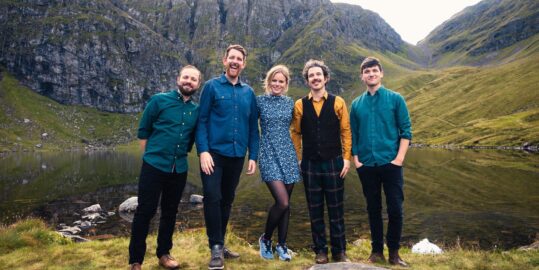 The five members of Breabach band outdoors with mountains in the background