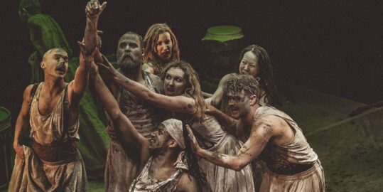 Cast on stage in worn-out white clothes covered in dirt