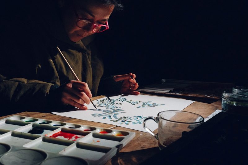 A woman wearing pink glasses, painting in a dark room