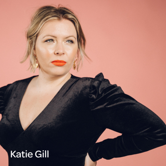 Image of woman in a black velvet top stood against a pink background
