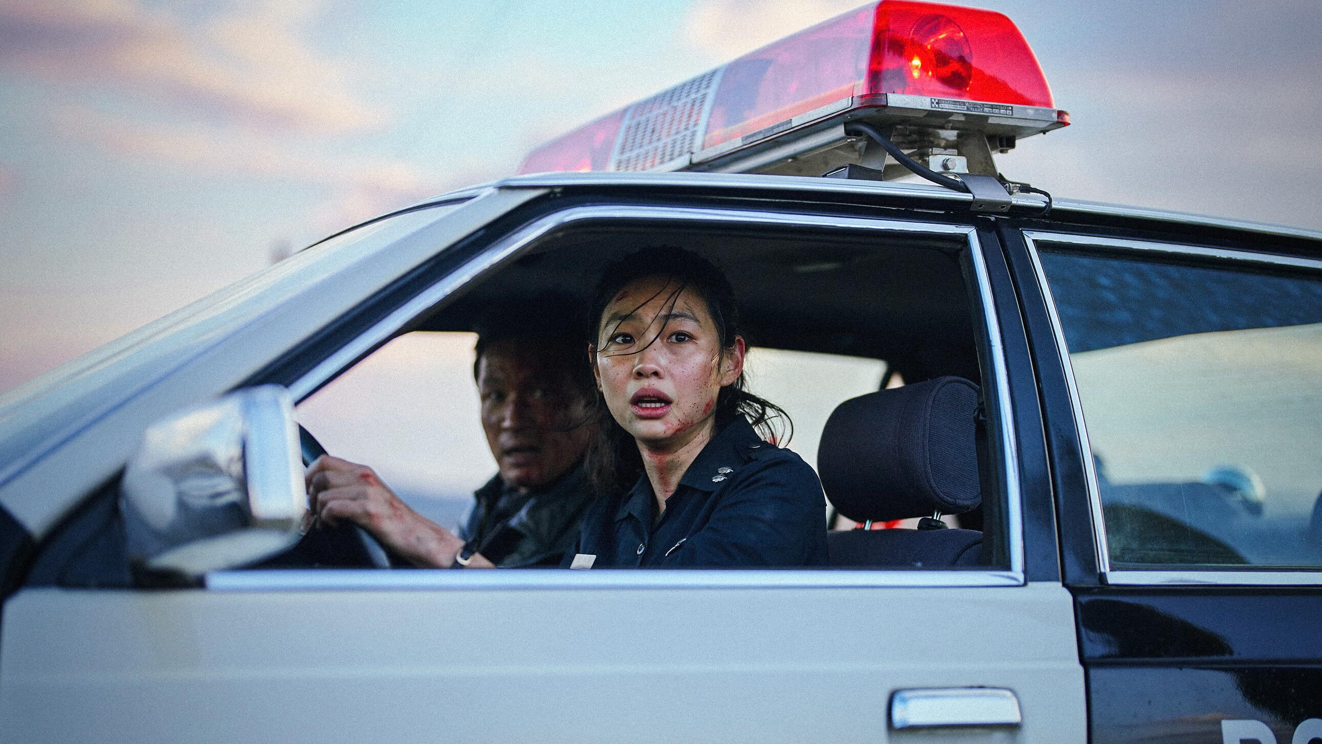 Two police officers in shock, one man and one woman in a police car looking out through the window